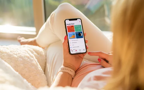 Photograph of a person holding a smartphone displaying a health data app with colorful sections for activity, heart rate, sleep, and mindfulness.