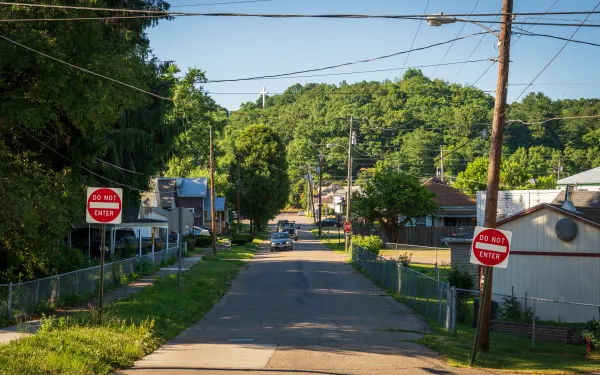 Photograph of a residential street in Nelsonville Ohio with two "Do Not Enter" signs on either side, indicating restricted access from this direction. The street is lined with houses, utility poles, and greenery, with a car visible in the distance under a clear blue sky.